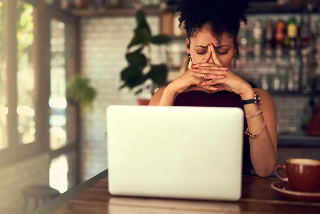 A woman feeling overwhelmed by anxiety looking at a laptop, seeking online mental health support.